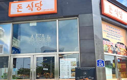 주황색 글씨로 돈 식당 061)335-9990 글씨가 적혀있고 오른쪽에는 김치찌개와 제육볶음 전문점이 적혀 있으며 음식 그림이 있다.