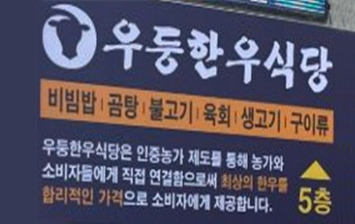 우동한우식당 간판 이미지. 한우 머리 모양의 로고 옆에 우동한우식당이라는 상호가 적혀 있고, 비빔밥·곰탕·불고기·육회·생고기·구이류 등의 메뉴가 안내되어 있다. 하단에는 우동한우식당은 인증농가 제도를 통해 농가와 소비자를 직접 연결하여 최상의 한우를 합리적인 가격으로 제공한다는 문구와 5층 위치 안내 표시가 있다.