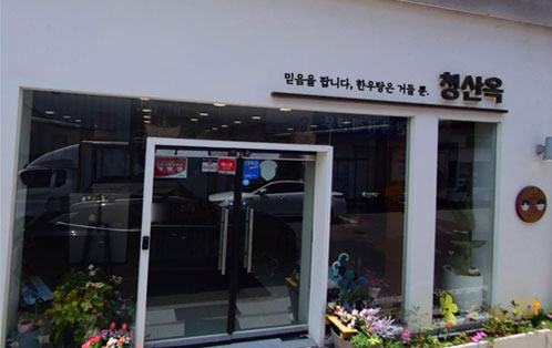 청산옥 식당 외부 전경. 흰색 외벽의 깔끔한 건물로, 입구 위에는 믿음을 팝니다. 한우물은 가를 줄.이라는 문구와 청산옥 간판이 걸려 있다. 유리문 출입구 앞에는 여러 화분이 놓여 있고, 내부에는 조명이 켜져 있다.