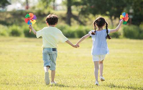 남자아이와 여자아이가 손잡고 한손에 바람개비를 들고 신나게 잔디위를 뛰고 있는 모습