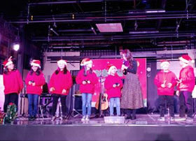 무대위에 어린이들이 빨간옷과 산타모자를 쓰고 나란히 서있는 모습
