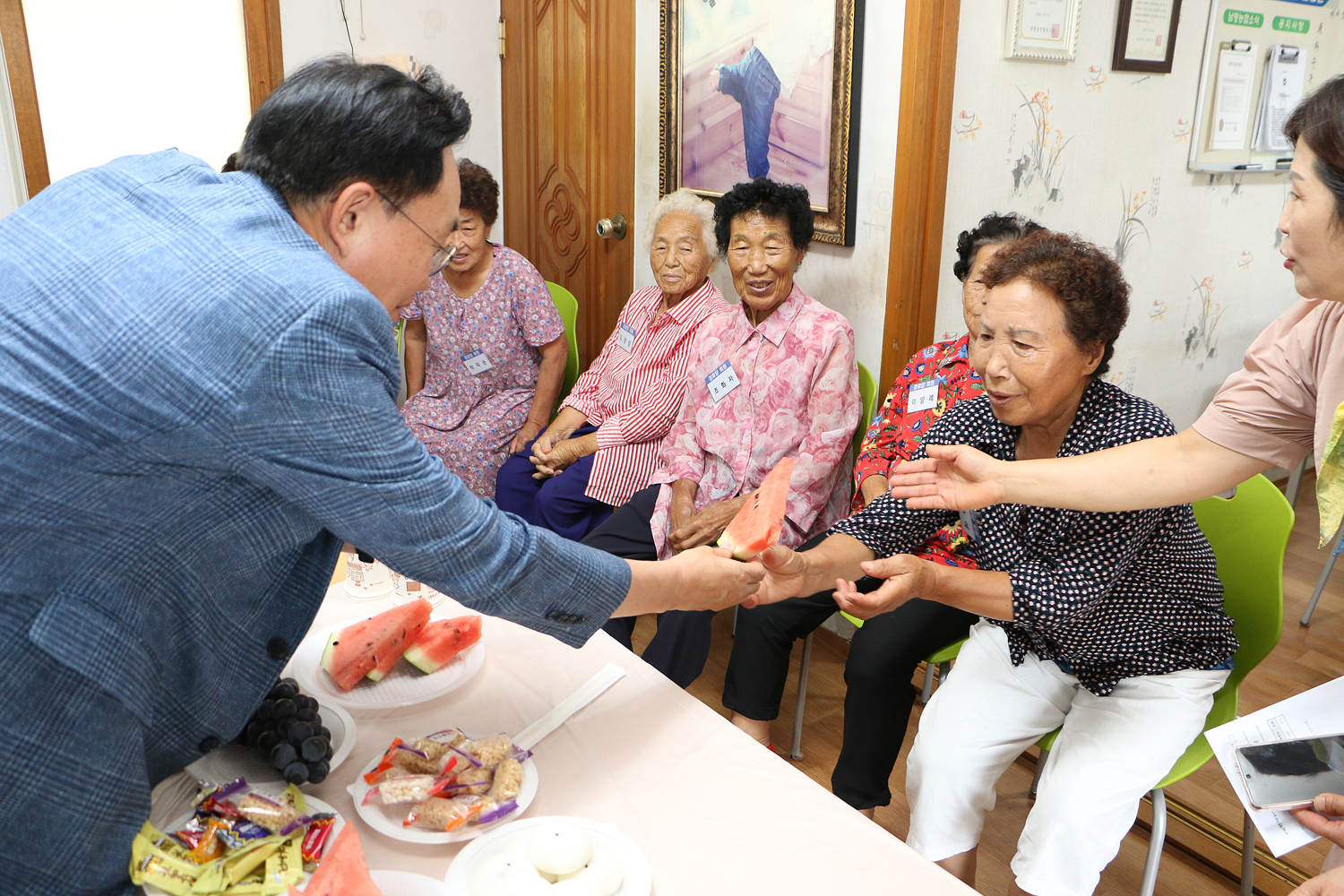 무더위 쉼터 현장 점검 나주시장이 마을 어르신들과 대화 중에 테이블에 놓인 수박 한조각을 여성 어르신께 드리고 있는 모습