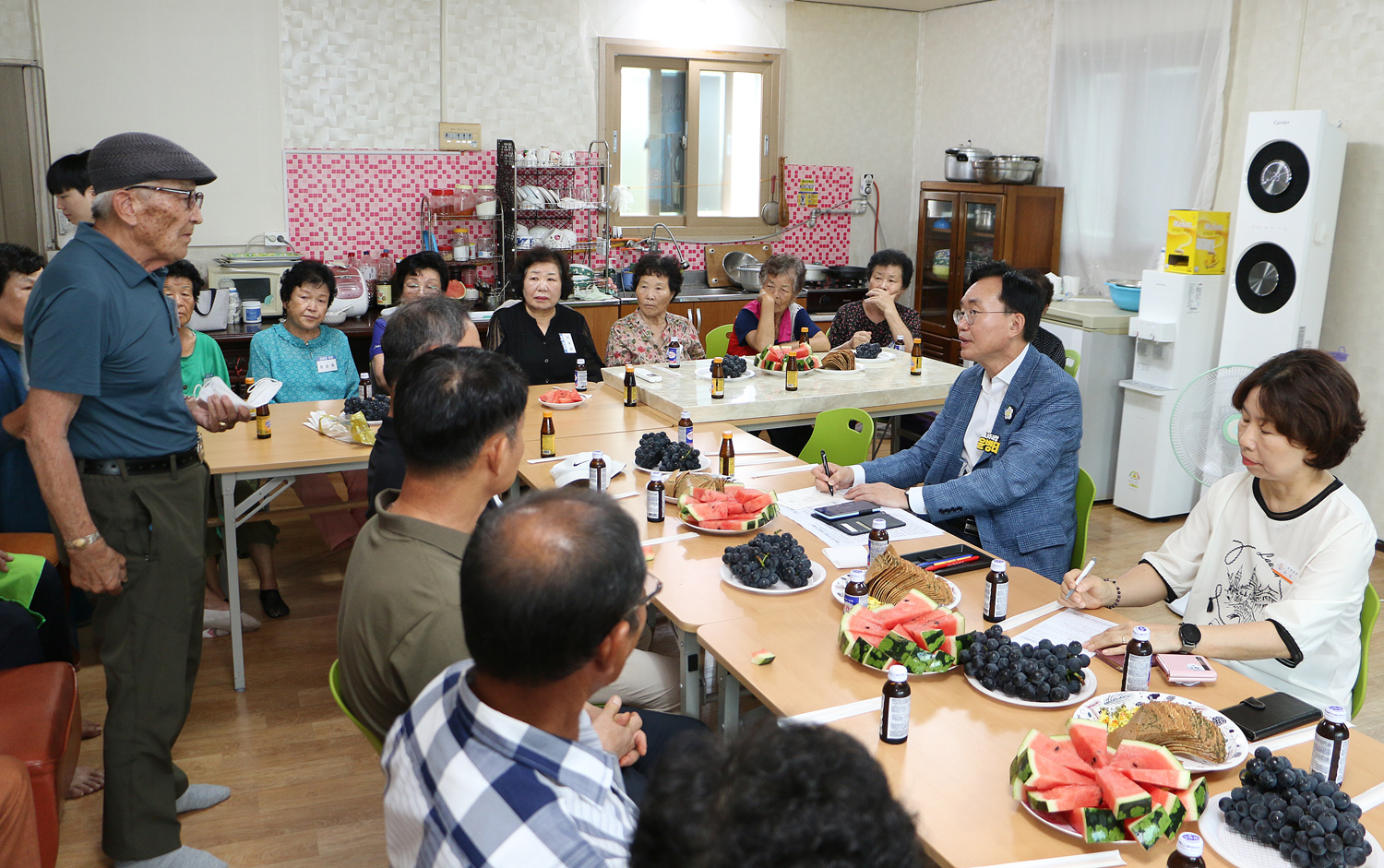 무더위 쉼터 현장 점검 테이블 뒷편에 앉아 있는 남성 어르신이 자리에 서서 나주시장에게 건의사항을 말하고 있고 자리에 앉은 나주시장이 한손에 펜을 들고 어르신읠 바라보며  경청하고 있는 모습