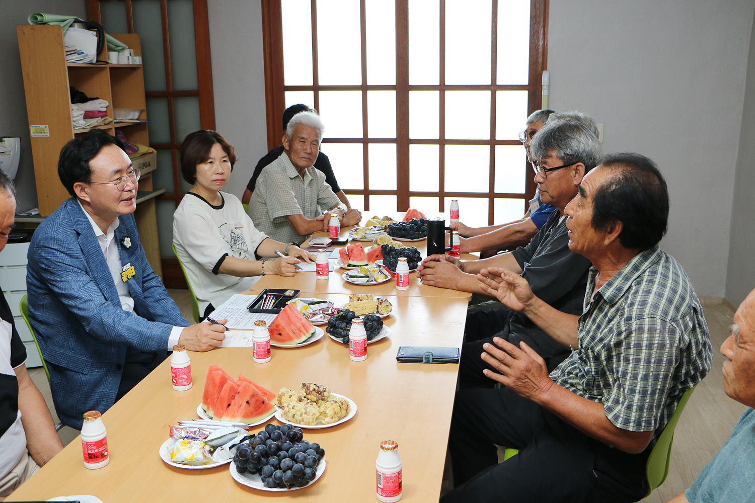 무더위 쉼터 현장 점검 나주시장과 마주 앉은 남성 어르신이 두팔을 들고 마을 역사를 설명하고 있고 한 손에 펜을 들고 어르신을 바라보며 경청하고  있는 나주시장의 모습