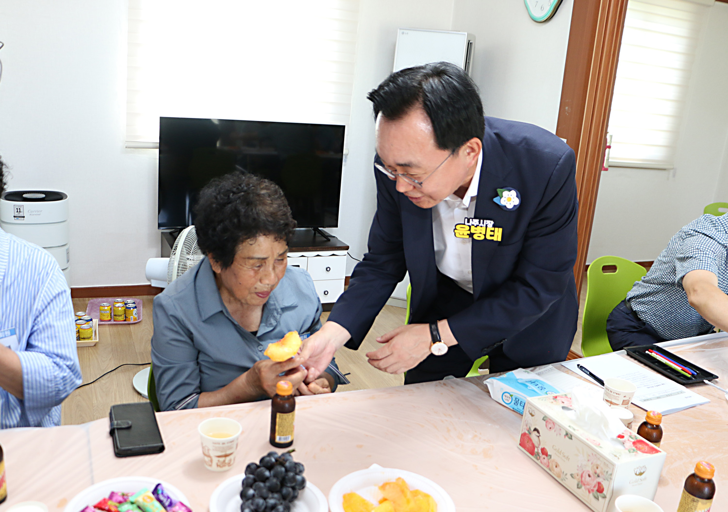 무더위 쉼터 현장 점검 나주시장이 자리에 반쯤 서서 바로 옆의 여성 어르신께 복숭아 한조각을 드리고 있는 모습