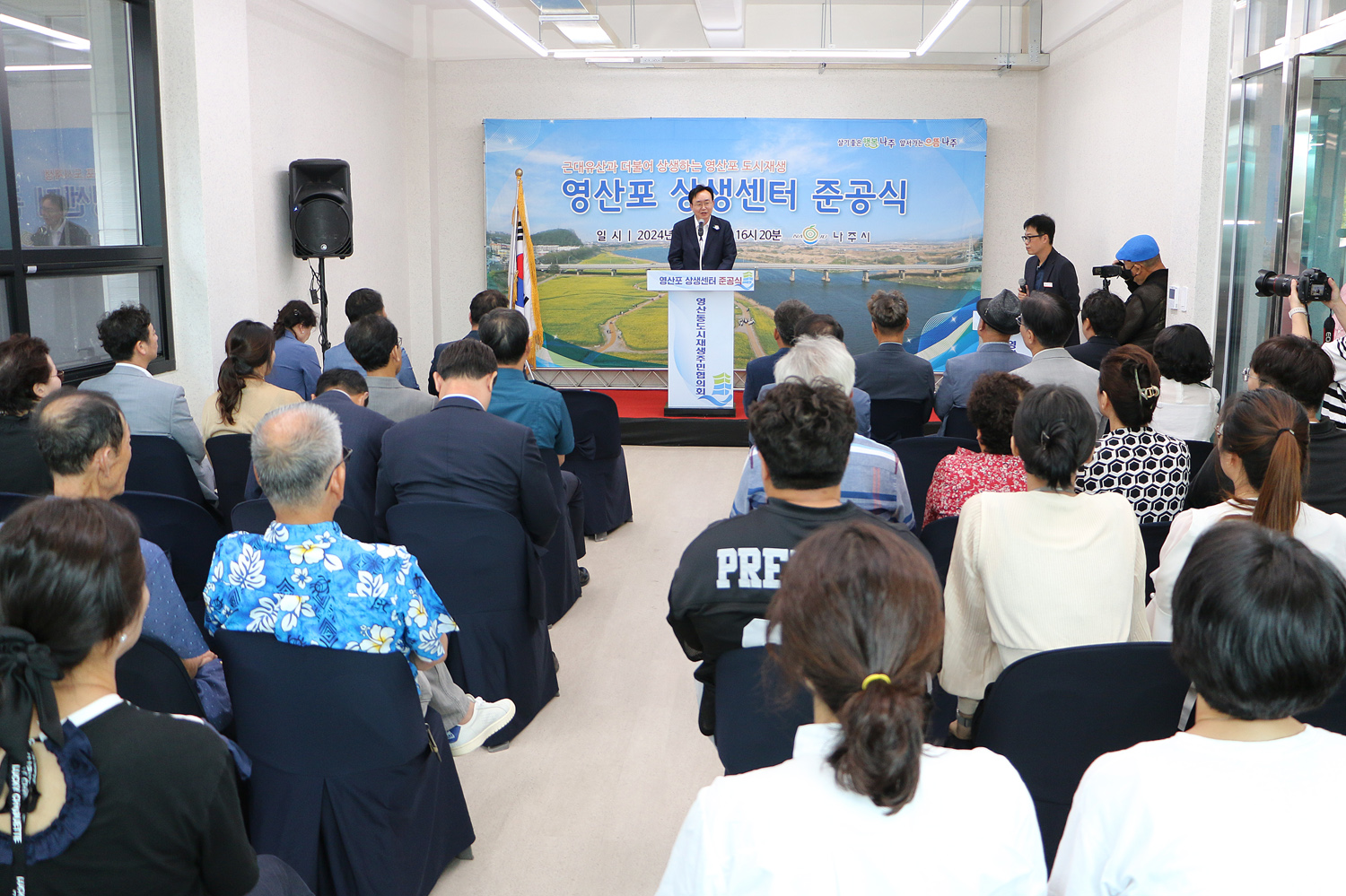 영산포 상생센터 준공식 나주시장의 축사모습과 자리에 앉아 있는 참석자들의 뒷모습 전면