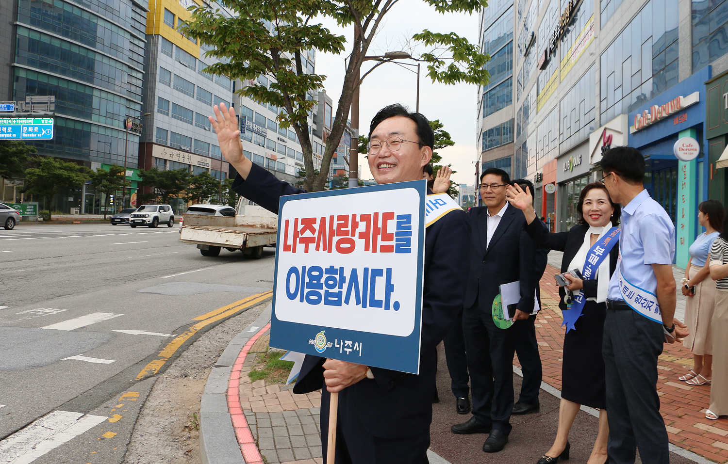 추석맞이 지역상품 판매 촉진 캠페인 및 청렴실천, 고향사랑 기부제 홍보 캠페인 나주시장이 나주사랑카드 이용 피켓을 들고 지나가는 차량을 향해 손을 흔들며 홍보켐페인을 벌이고 있는 모습