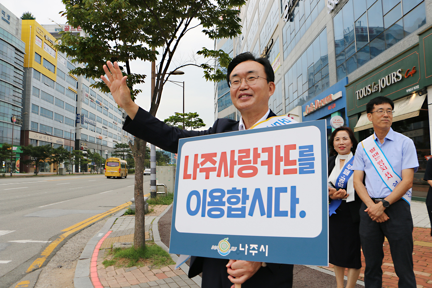 추석맞이 지역상품 판매 촉진 캠페인 및 청렴실천, 고향사랑 기부제 홍보 캠페인 나주시장이 얼굴에 미소를 지으며 나주사랑카드 이용 피켓을 들고 한손은 이동차량을 향해  손을 흔들며 홍보 캠페인을 하고 있는모습