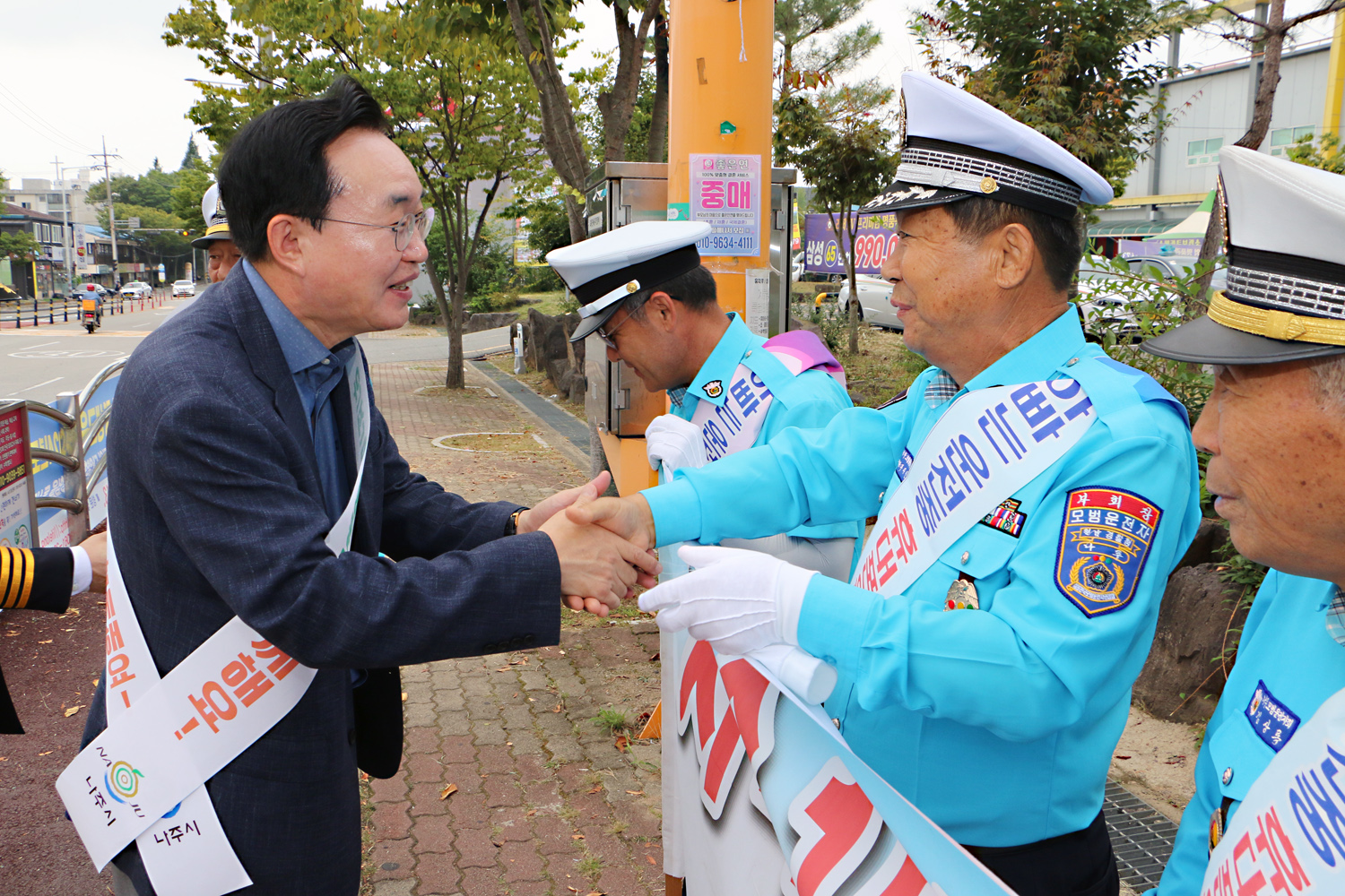 민, 관, 경 합동 어린이 교통안전 캠페인 나주시장이 모범운전자회 남성 회원분의 한손을 두손으로 맞잡고 인사를 나누는 모습