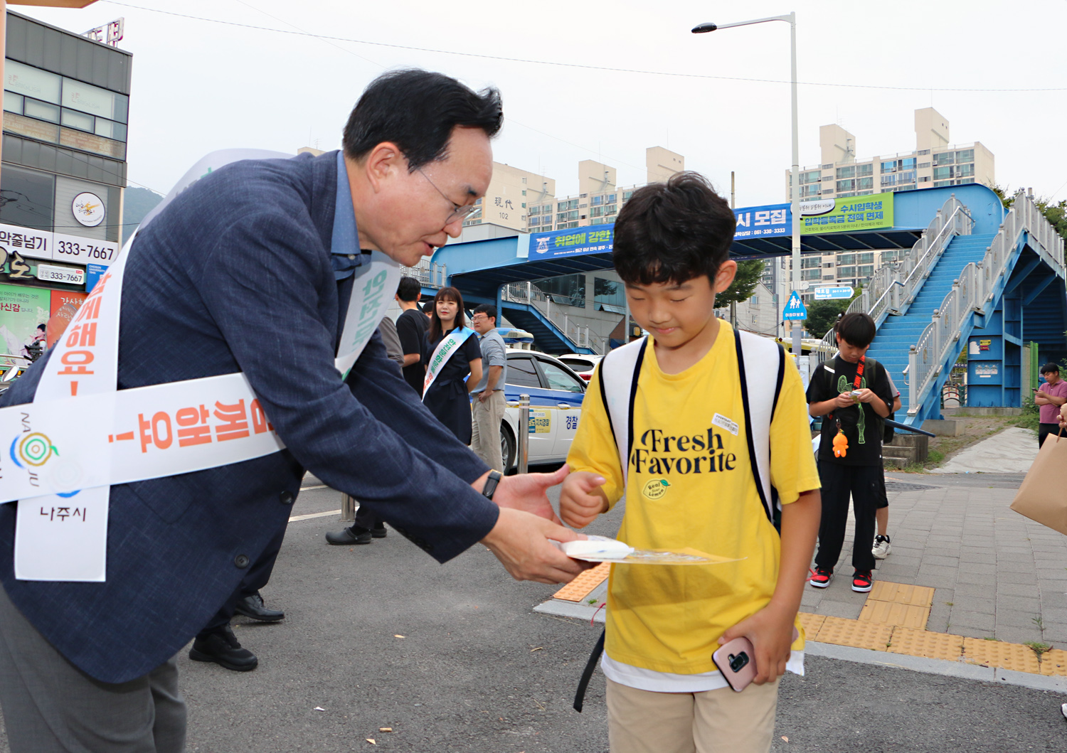 민, 관, 경 합동 어린이 교통안전 캠페인 나주시장이 중앙초교 앞에서 등교를 하고 있는 남자 어린이에게 홍보 전단지를 전달하고 있는 모습