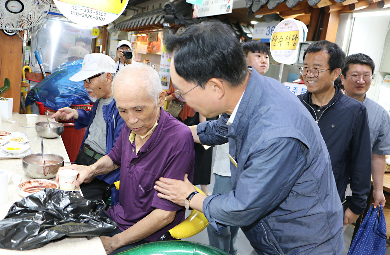 추석 명절맞이 나주목사고을시장 장보기 행사 나주시장이 팥죽가게에서 팥죽을 다 먹고 물을 마실려는 남성 어르신의 어깨와 팔을 잡으며 인사를 나누는 모습