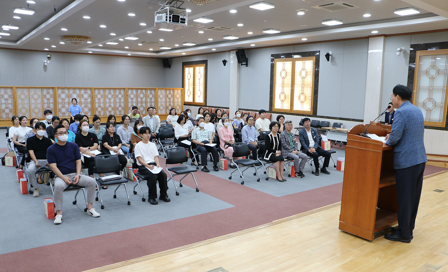 나주시 어린이 사회복지 급식관리지원센터 사업설명회 인사말을 하고 있는 나주시장의 뒷편에서 촬영한 사진 참석자들이 앉아서 듣고 있는 모습이 보인다