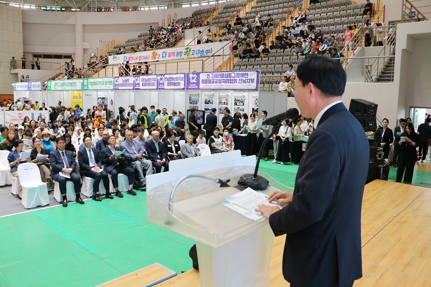 2024 전라남도 장애인 일자리 박람회 나주시장이 환영사를 하고 있는 뒷편에서 촬영한 사진 참석자들의 앞모습이 보인다