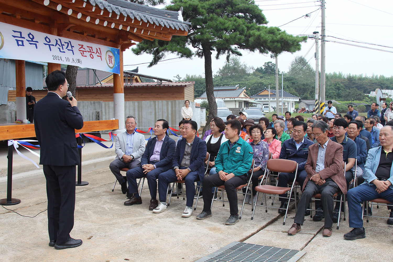 문평면 옥당리 금옥마을 우산각 준공식 축사를 하고 있는 나주시장의 뒷편에서 촬영한 축사모습 참석자들의 앉아 있는 모습이 보인다