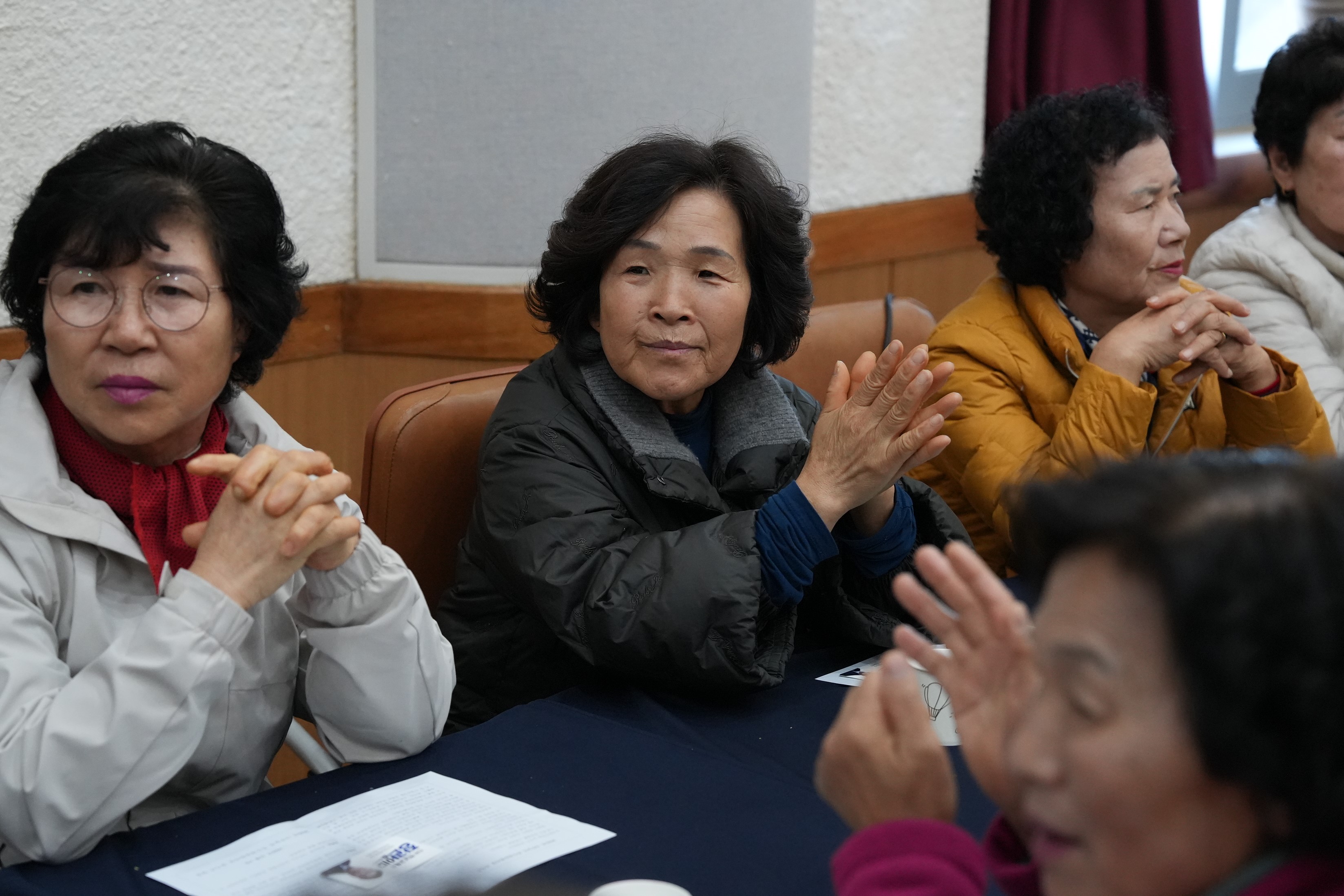 행사에 참석한 중년 여성들 여러 명이 테이블에 앉아 박수를 치거나 주의 깊게 경청하고 있는 모습