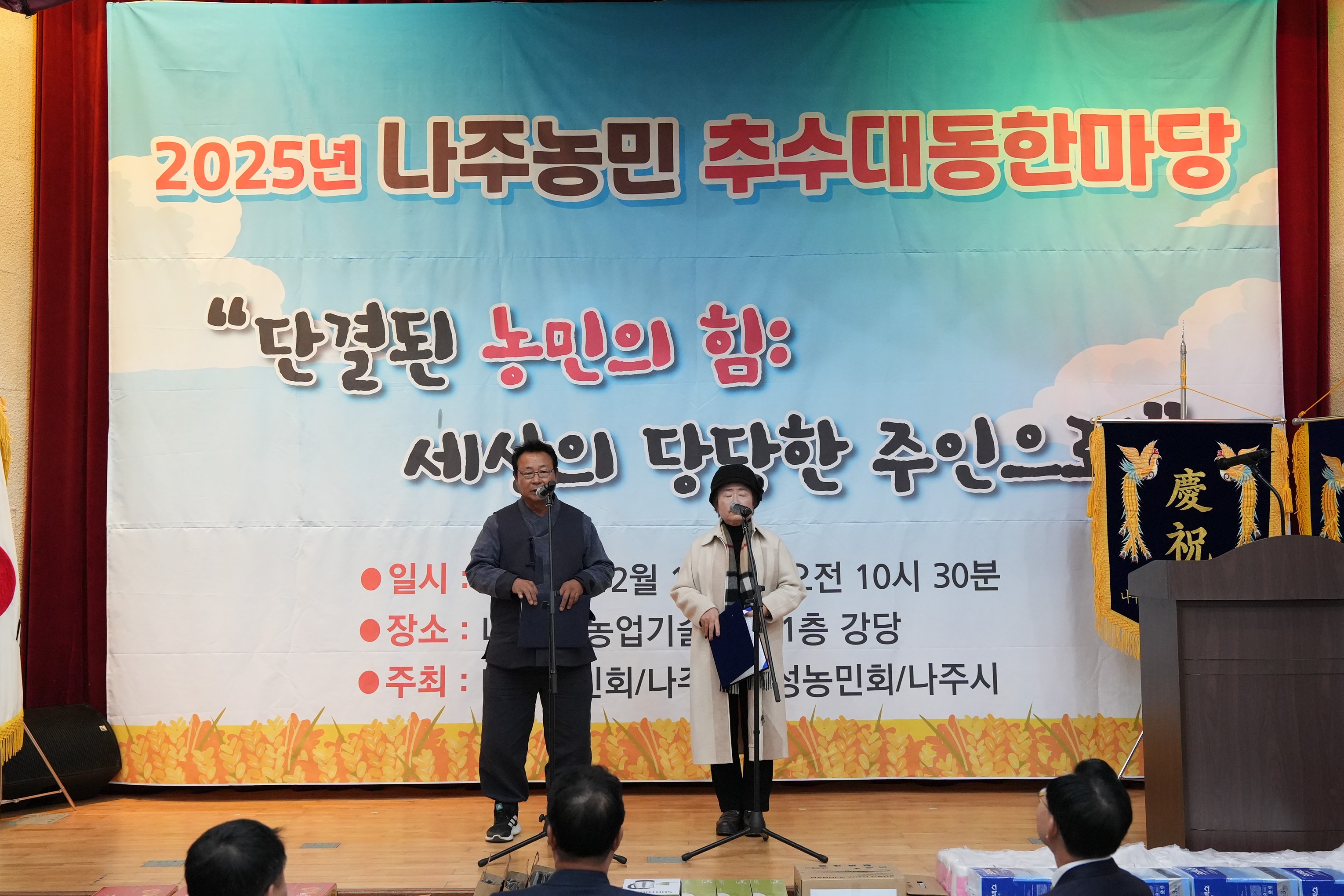 '2025년 나주농민 추수대동한마당' 무대 위에서 중년 남녀 두 명이 마이크 앞에서 순서를 진행하고 있는 모습