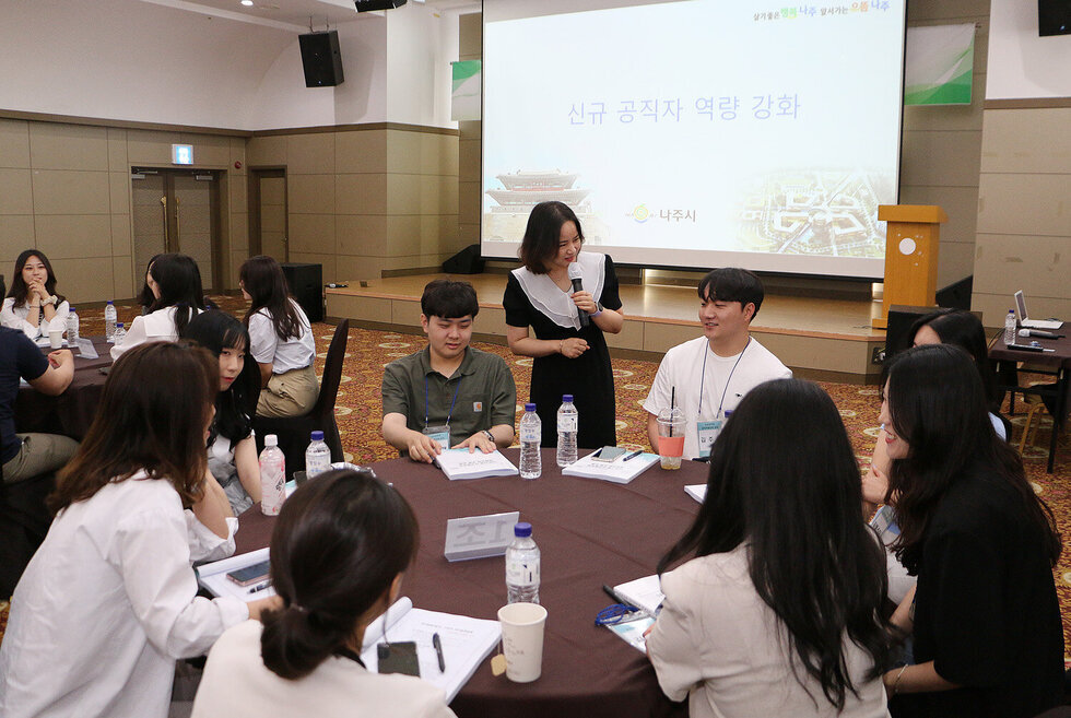 신규임용자 공직역량 강화 교육 원형테이블에 앉아 있는 직원들과 강사가 서서 대화를 나누고 있는 모습