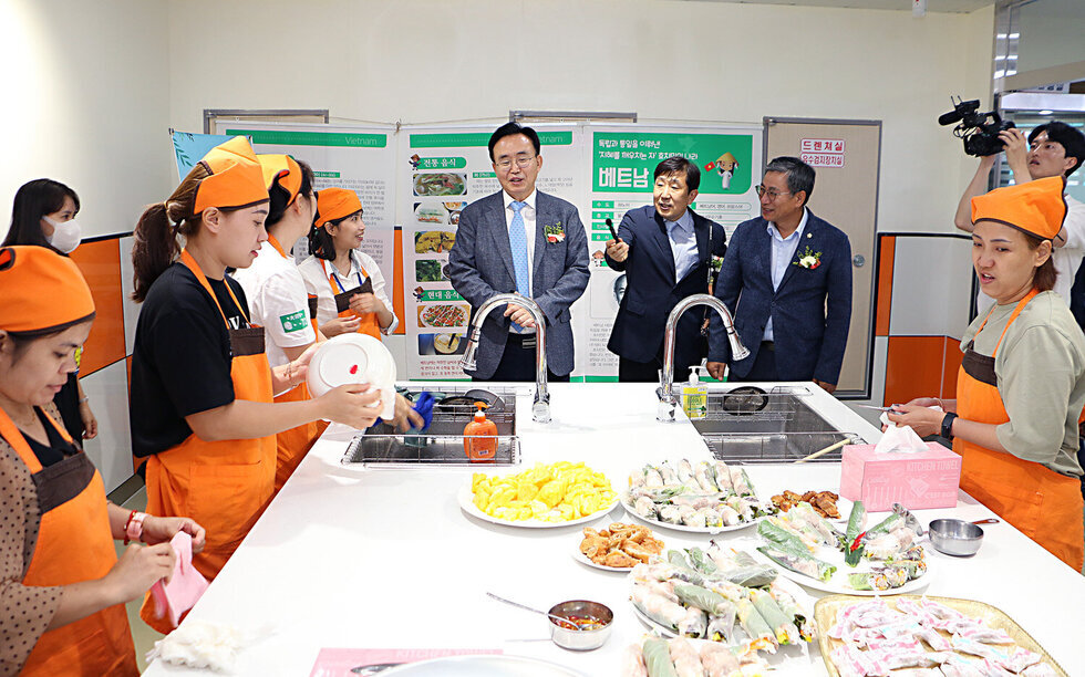 나주시 가족센터 개소식 나주시장이 나주시 가족센터장과 함께 시설 투어 중 다문화 음식을 만드는 여성분들에게 인사말을 하고 있는 모습