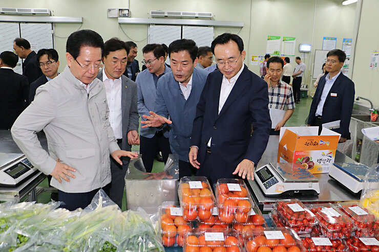 친환경농산문 종합물류센터 전남도지사 방문 전남도지사와 나주시장이 농산물을 바라보고 있고 관계자가 중간에 서서 설명을 하고 있는 모습