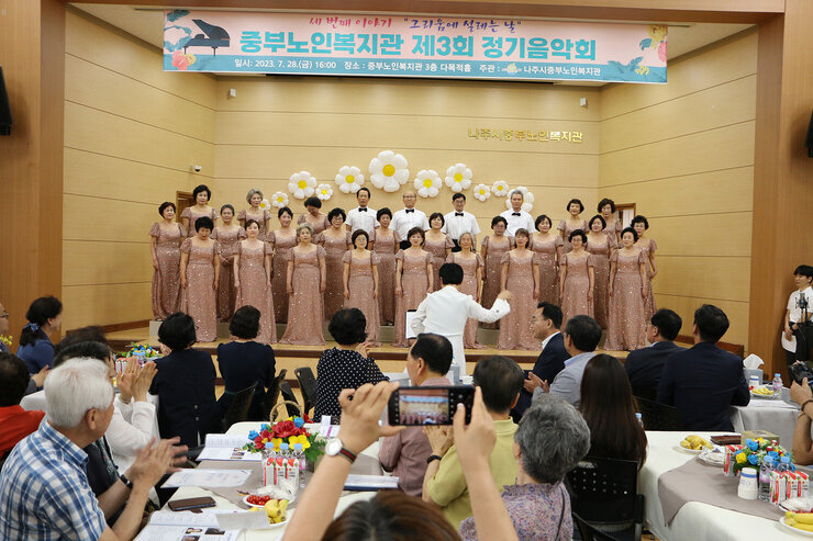 중부노인복지관 제3차 정기음악회 합창단의 공연 모습과 지휘자가 앞에서 지휘를 하고 있는 모습
