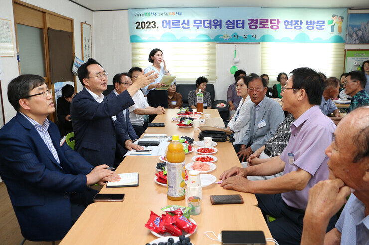 세지면 무더위 쉼터 방문 자리에 앉아서 나주시장이 남성 어르신의 질문에 팔을 들어올리며 설명을 하고 있는 모습
