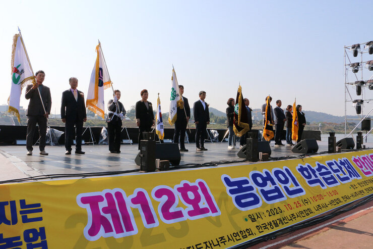 제12회 농업인 학습단체 한마음대회 농업관련 단체들의 기를 들고 있는 관계자들이 무대 위에 서 있는 모습
