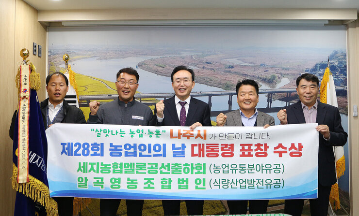 제28회 농업인의 날 대통령 표창 수상 나주시장과 세지농협 조합장, 알곡영농조합 법인 대표 및 관계자 2명이 플래카드를 펼치고 기념촬영을 하고 있는 모습