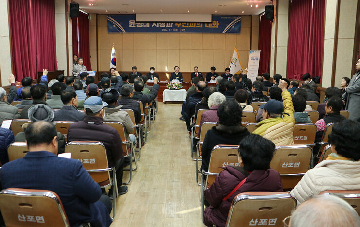산포면 주민과의 대화  나주시장과 면장 간부공무원, 시의원이 대화석에 앉아 있고 질문을 하기위해 주민들이 손을 들고 있는뒷 모습