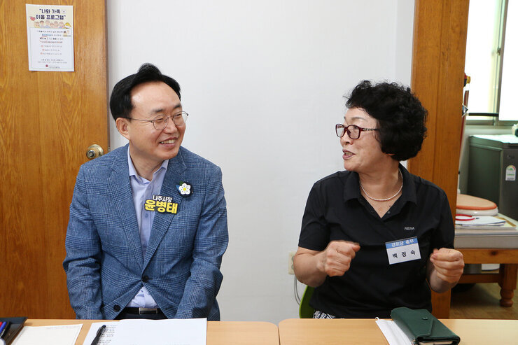 무더위 쉼터 현장 점검 입식테이블 자리에 앉아 있는 나주시장이 바로 옆에 앉아 있는 여성 어르신과 마주보며 미소를 머금고 대화를 나누는 모습