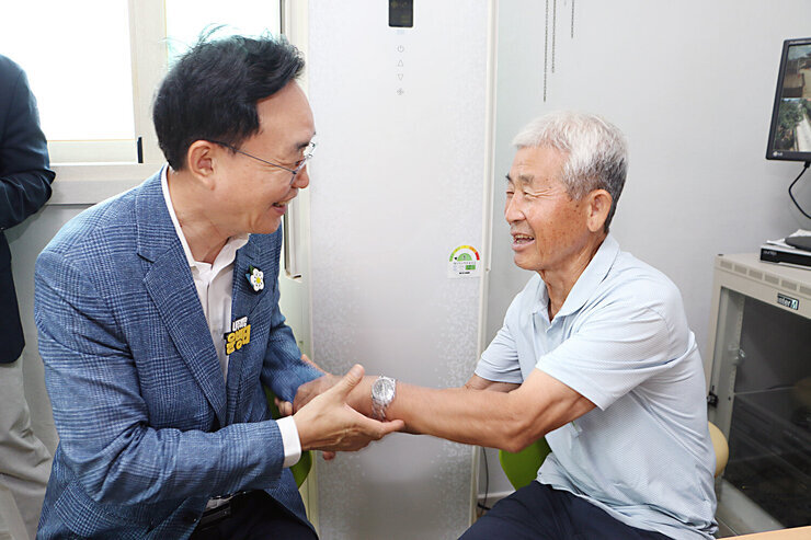 무더위 쉼터 현장 점검 나주시장이 옆에 앉아 있는 남성 어르신의 한손을 두손으로 잡으며 미소를 짓고 있는 모습