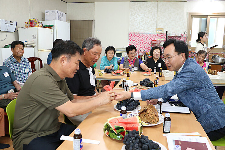 무더위 쉼터 현장 점검 입식테이블에 앉아 있는 나주시장이 마주 앉은 남성 어르신게 수박 한조각을 드리고 있는 모습