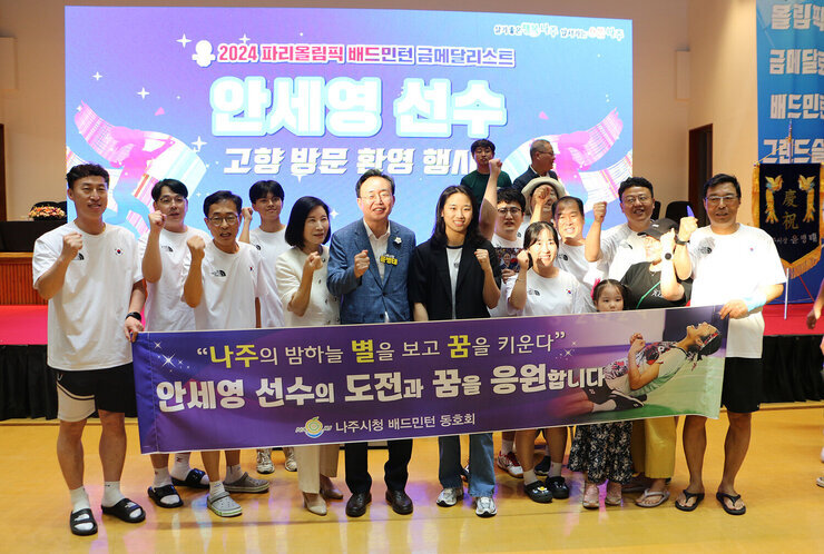 파리올림픽 금메달리스트 안세영 선수 나주 환영행사 안세영 선수와  나주시장이 나주시청 배드민턴 동호회 회원과 현수막을 펼치고 기념촬영을 하고 있는 모습