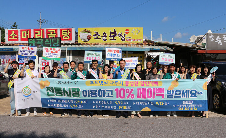추석 명절맞이 영산포 풍물시장 장보기 행사 나주시장과 시청 담당 부서 직원 등이 전통시장 이용 페이백의 내용의 현수막을 펼치고 화이팅을 하며 기념촬영을 하고 있는 모습