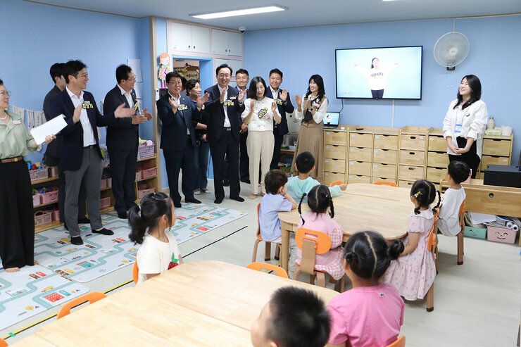 나주시 365일 시간제 보육실 개원식 보육실 안의 아동들이 동요를 부르고 있고 나주시장과 배우자 및 관계자들이 서서 박수를 쳐주고 있는 모습
