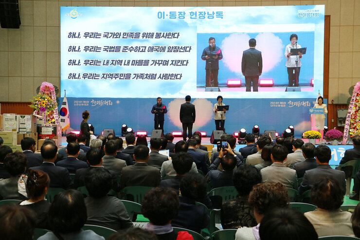 제6회 이, 통장 한마음대회 무대 위 에서 남성, 여성 대표자가 헌장 낭독을 하고 있는 모습과 참석자들이 앉아 있는 뒷모습