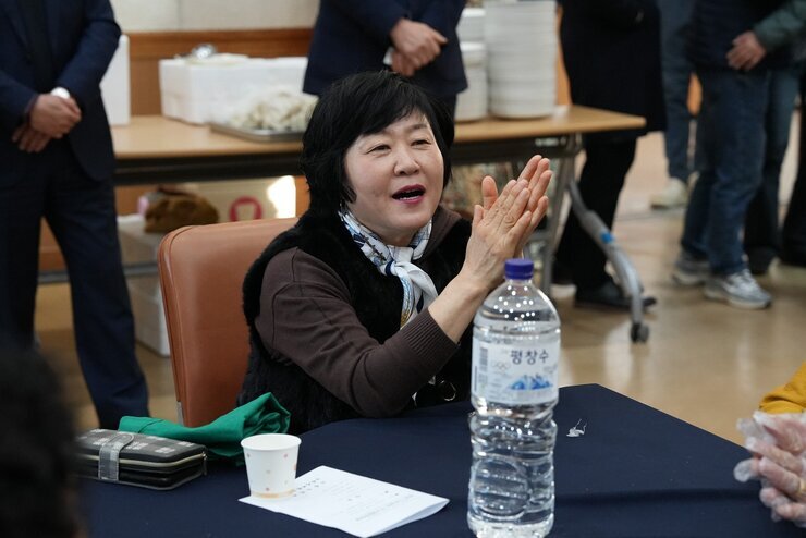  행사에 참석한 중년 여성이 테이블에 앉아 손뼉을 치며 환하게 웃고 있는 클로즈업 사진