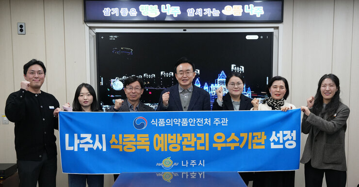  윤병태 나주시장(가운데)과 시청 직원들로 보이는 남녀 7명이 '식품의약품안전처 주관 나주시 식중독 예방관리 우수기관 선정 나주시'이라고 적힌 파란색 현수막을 들고 기념사진을 찍고 있는 모습. 모두 주먹을 쥐고 있다.