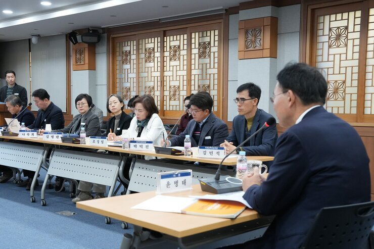  회의 또는 간담회 장면. 테이블에는 참석자들이 앉아 자료를 검토하거나 경청하고 있다.