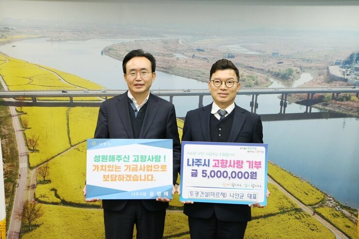 왼쪽에 시장님이 성원해주신 고향사랑! 가치있는 기금사업으로 보답하겠습니다. 라고 적힌 팻말을 들고 오른쪽에 나주시 고향사랑 기부 금 5,000,000원 토광건설(미르채) 나안균 대표라고 적힌 팻말을 들고 기념 촬영 중이다