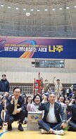 나주시배구협회장배 고등학교 남녀 배구대회 나주시장과 배구협회장 및 내빈들이  배구 코트 바닥에 앉아서 한손을 올리고 화이팅을 외치며 기념촬영을 하고 있는 모습