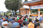 문평면 옥당리 금옥마을 우산각 준공식 나주시장이 우산각 옆에서 축사를 하고 있고 참석자들이 앉아 있는 뒷모습