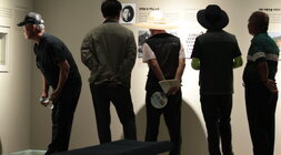 정면을 응시하는 소년와 같은 글귀와 사진들이 벽에 붙어있는 전시회를 보는중인 의회원들