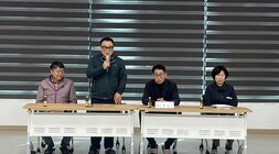 테이블에 앚아있는 위원회원들과 서서 발표중인 위원회원