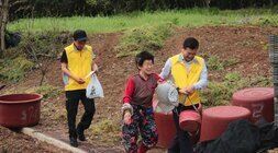 할머니를 부축하며 걸어가는 봉사자와 반찬을 들고 뒤를 따라가는 봉사자