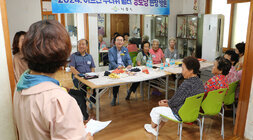 무더위 쉼터 현장 점검 입식테이블 뒷편에 서 있는 경로당 총무 여성분이 나주시장에게 건의사항을 말하고 있는 뒷모습과 나주시장이 자리에 앉아 듣고 있는 모습 마을 어르신들이 앉아 있는 모습도 보인다