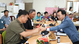 무더위 쉼터 현장 점검 입식테이블에 앉아 있는 나주시장이 마주 앉은 남성 어르신게 수박 한조각을 드리고 있는 모습