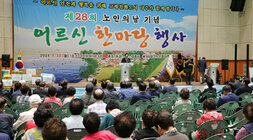 제28회 노인의 날 어르신 한마당 개막식 좌측면에서 촬영한 나주시장의 축사모습과 참석 어르신들의 앉아 있는 뒷모습