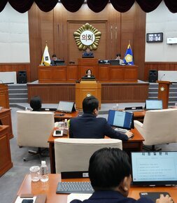 시의회 본회의장 전경. 의원들이 책상에 앉아 있고, 중앙 단상에서 발언하는 사람이 있으며, 벽면 스크린에는 '의회' 글자와 회의 내용이 보임