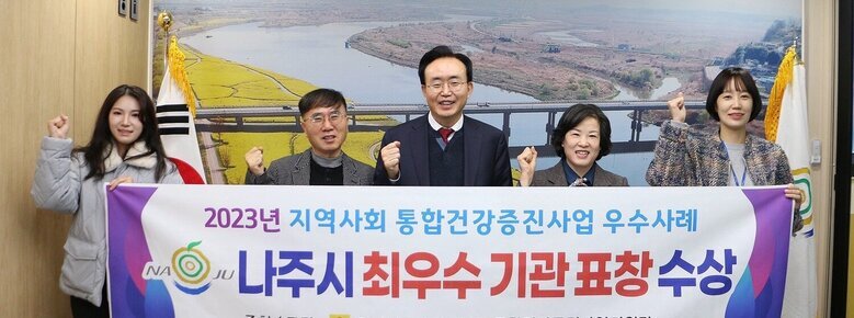 2023년 통합건강증진사업 우수사례 선정 관련 나주시장과 보건소장 담당부서 직원들이 플래카드를 펼치고 기념촬영을 하고 있는 모습